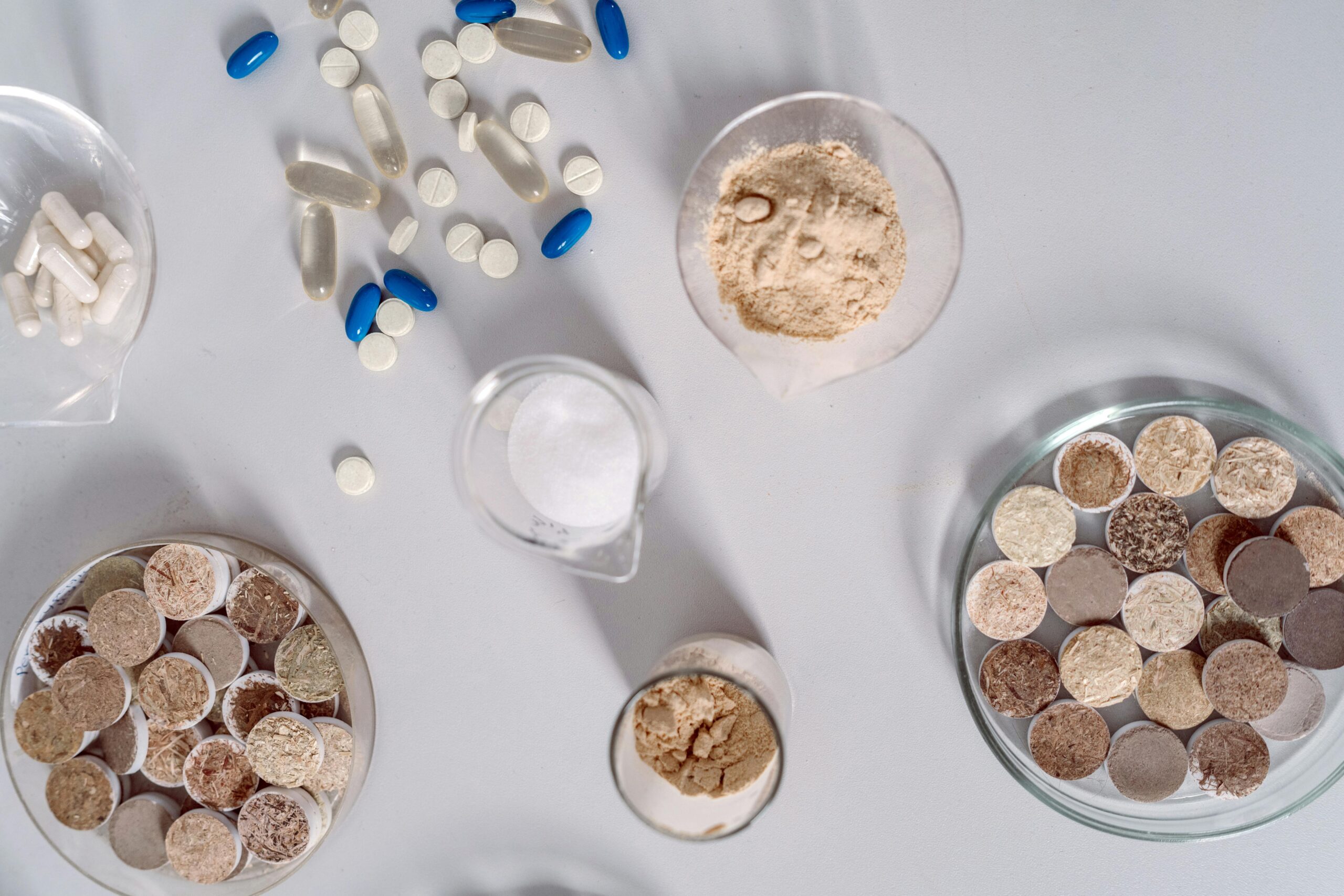 High-angle shot of various pharmaceutical ingredients and pills on a white surface. Ideal for healthcare and science themes.